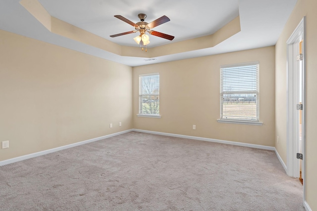 carpeted spare room featuring a raised ceiling, ceiling fan, and a healthy amount of sunlight