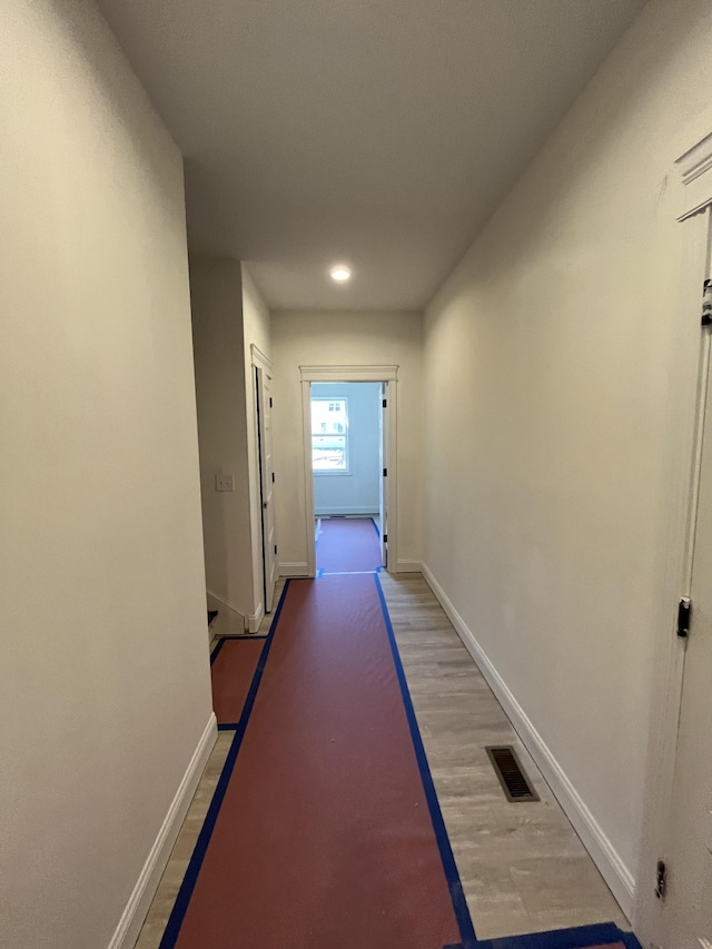 corridor with light wood-type flooring, visible vents, and baseboards