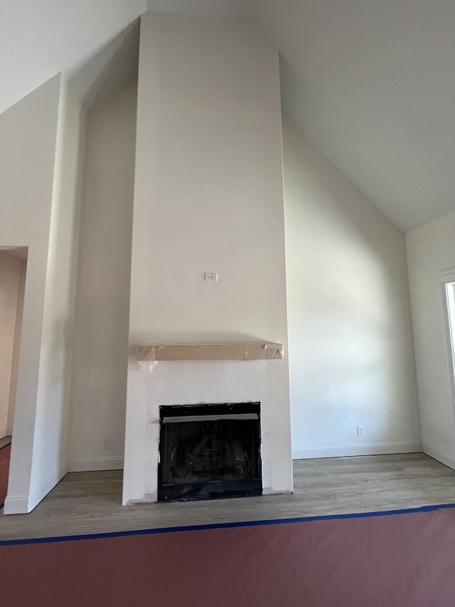 unfurnished living room with lofted ceiling, a fireplace, wood finished floors, and baseboards