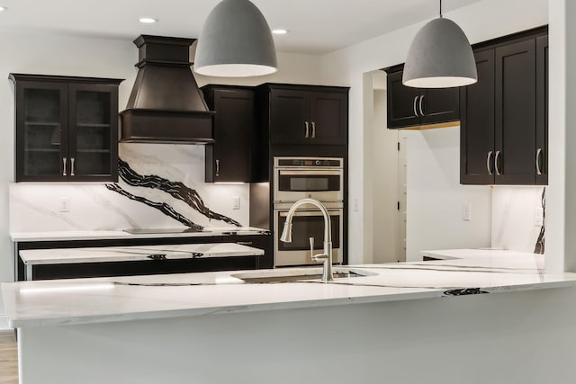 1049 Gholson Rd, Clarksville, TN 37043 - kitchen with stainless steel double oven, light stone counters, dark cabinets, decorative backsplash, and custom exhaust hood