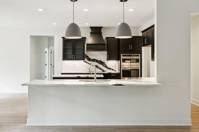 1049 Gholson Rd, Clarksville, TN 37043 - kitchen with stainless steel double oven, baseboards, light wood-style flooring, hanging light fixtures, and custom exhaust hood