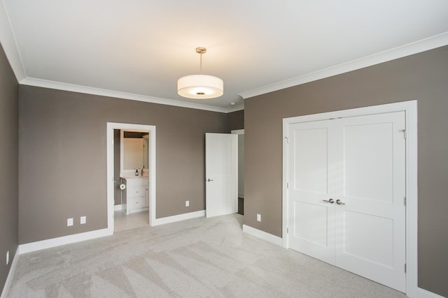 unfurnished bedroom featuring light carpet, baseboards, ornamental molding, a closet, and ensuite bath