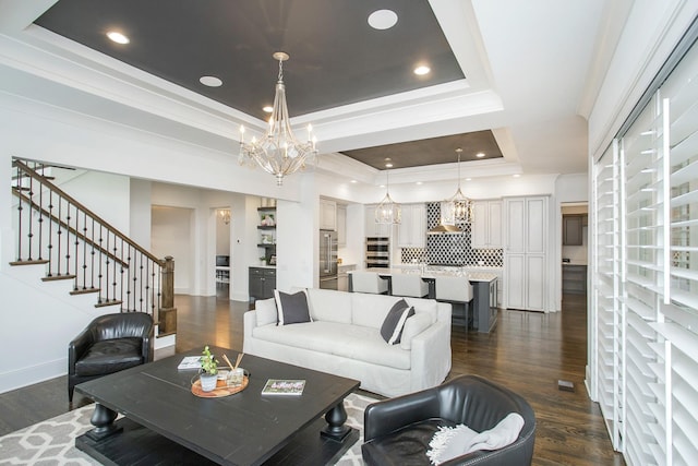 living area with stairway, a raised ceiling, dark wood-style flooring, and a chandelier