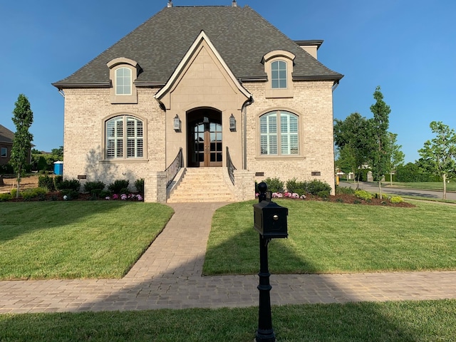 french provincial home featuring french doors, brick siding, and a front lawn