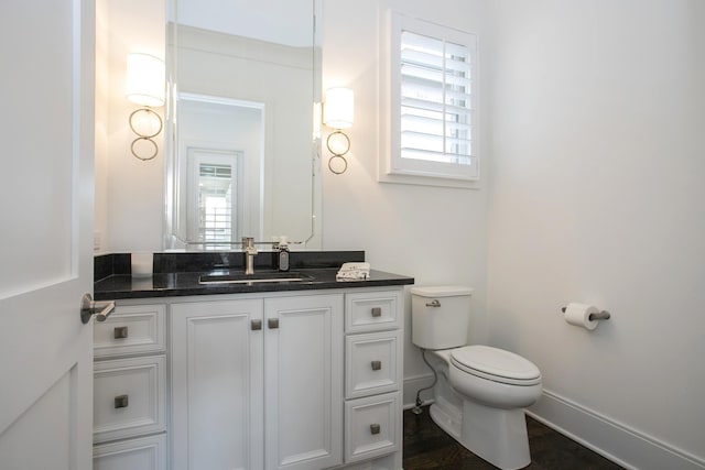 half bathroom featuring toilet, vanity, a wealth of natural light, and baseboards