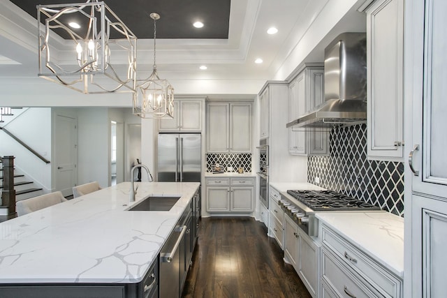 kitchen featuring a large island, appliances with stainless steel finishes, dark wood-style flooring, wall chimney range hood, and a sink