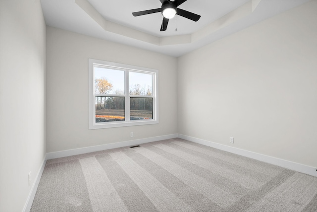 unfurnished room with a raised ceiling, ceiling fan, and carpet flooring