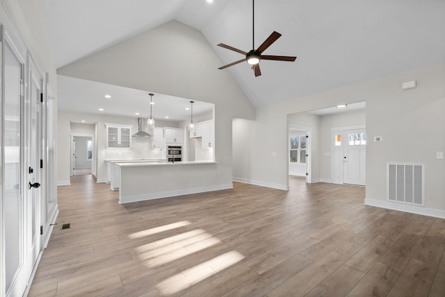 unfurnished living room with light hardwood / wood-style floors, high vaulted ceiling, and ceiling fan