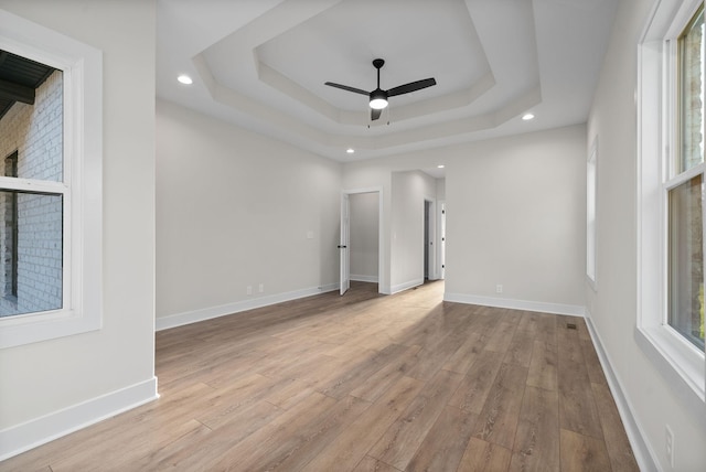 empty room featuring a tray ceiling, ceiling fan, and light hardwood / wood-style flooring