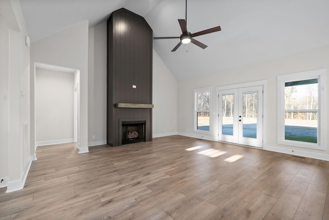 unfurnished living room with ceiling fan, a large fireplace, french doors, high vaulted ceiling, and light wood-type flooring