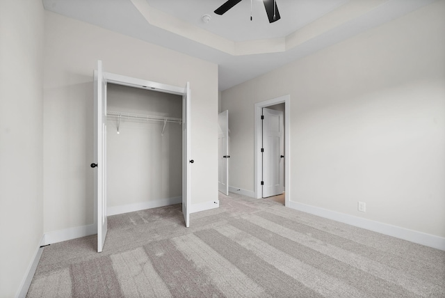 unfurnished bedroom with ceiling fan, a raised ceiling, light carpet, and a closet