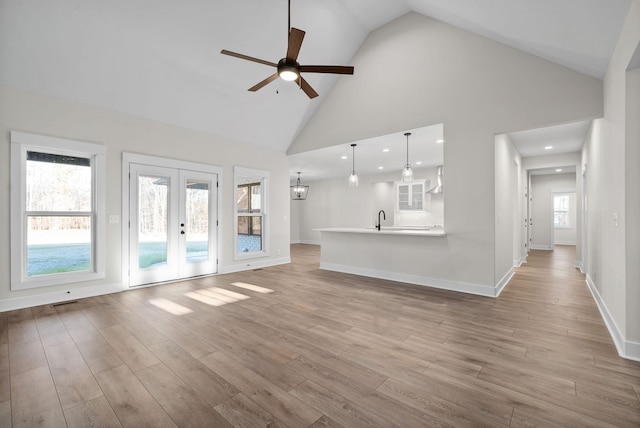 unfurnished living room with french doors, light wood-type flooring, ceiling fan, sink, and high vaulted ceiling