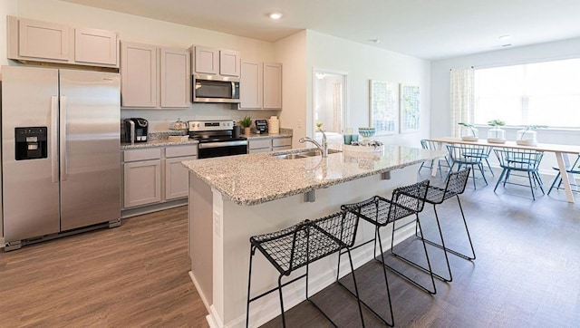 kitchen with light stone countertops, appliances with stainless steel finishes, a kitchen island with sink, dark hardwood / wood-style floors, and a breakfast bar area