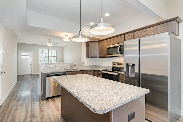 kitchen featuring pendant lighting, a center island, sink, appliances with stainless steel finishes, and light hardwood / wood-style floors