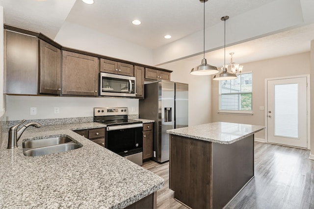 kitchen with sink, light stone counters, dark brown cabinets, a kitchen island, and appliances with stainless steel finishes