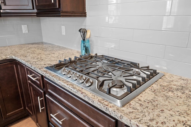 kitchen with tasteful backsplash, light stone counters, dark brown cabinets, and stainless steel gas stovetop