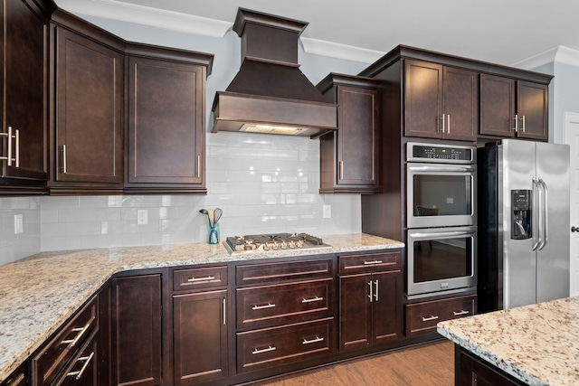 kitchen with stainless steel appliances, premium range hood, light hardwood / wood-style floors, dark brown cabinets, and ornamental molding