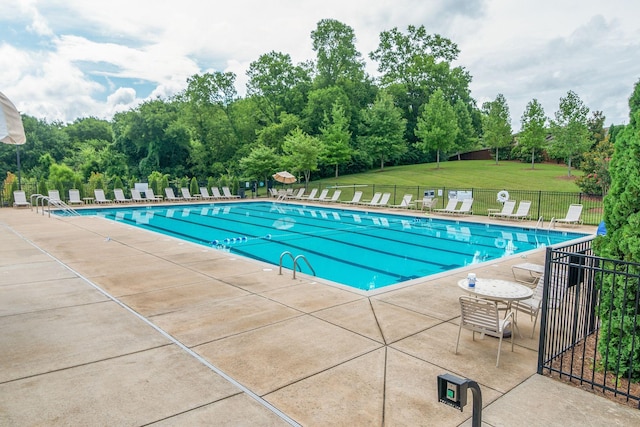 pool with a patio, a lawn, and fence