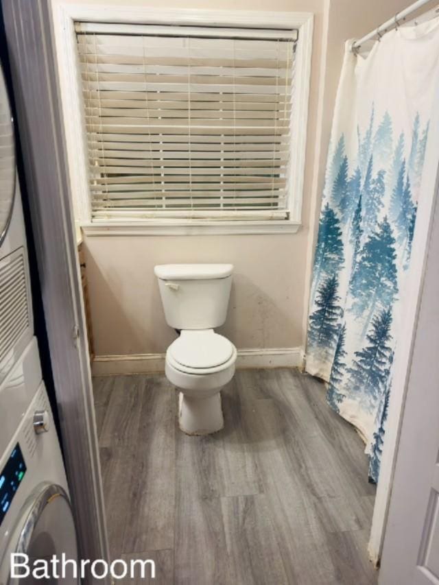 bathroom featuring wood-type flooring, stacked washing maching and dryer, and toilet