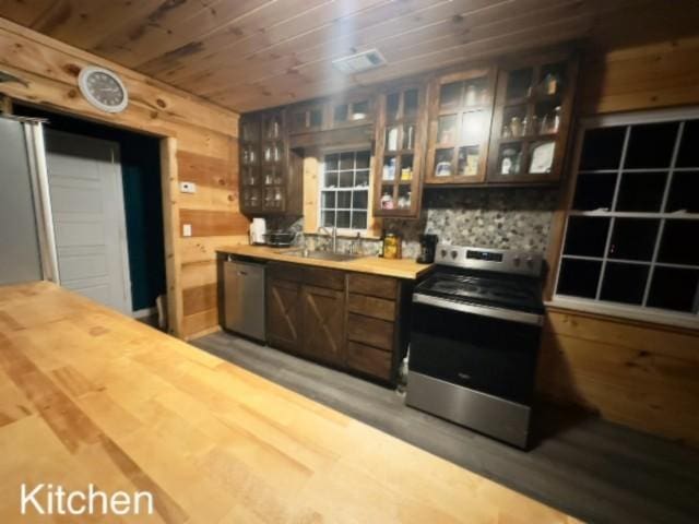 kitchen featuring wood walls, sink, appliances with stainless steel finishes, dark brown cabinets, and wood-type flooring