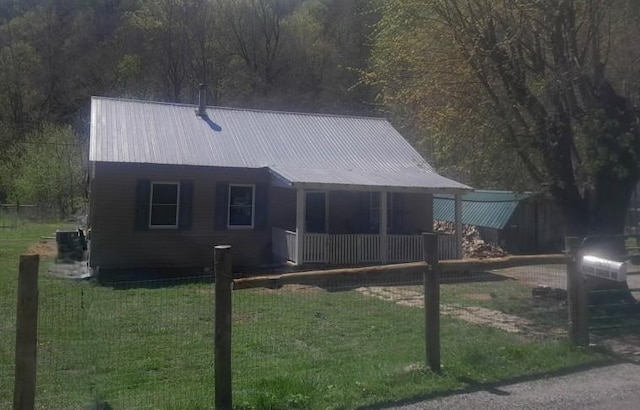 rear view of property with central AC, metal roof, covered porch, a lawn, and a fenced front yard