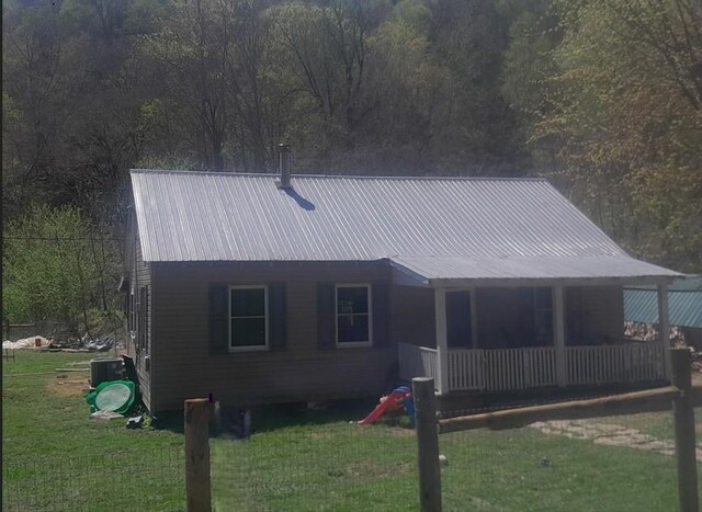 exterior space with a yard, a wooded view, cooling unit, and metal roof