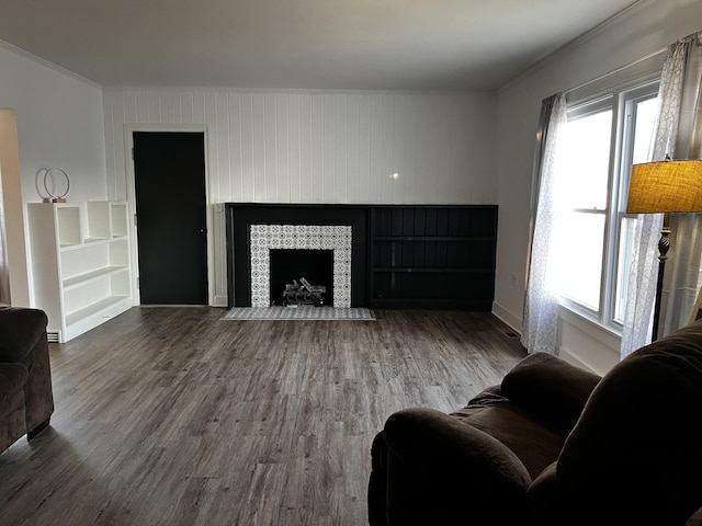 living room with wood walls, wood-type flooring, ornamental molding, and a tile fireplace