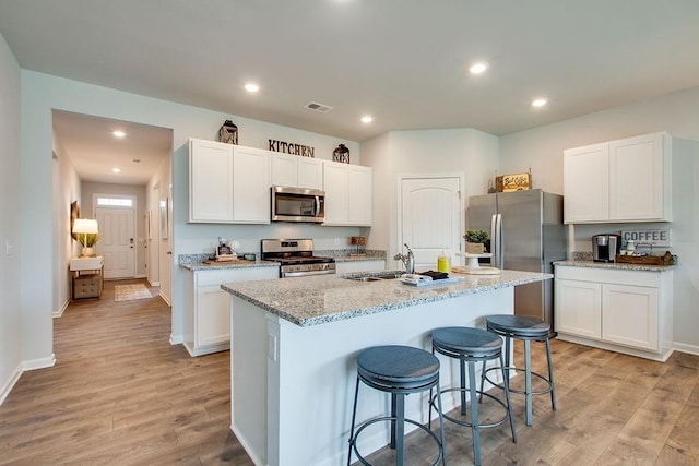 kitchen with appliances with stainless steel finishes, light hardwood / wood-style floors, a kitchen island with sink, and sink