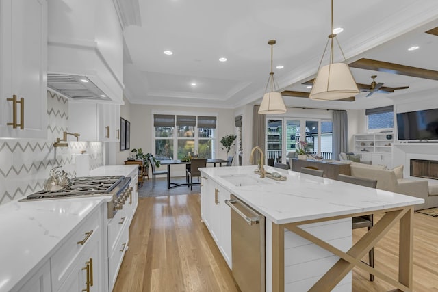 kitchen featuring premium range hood, white cabinets, an island with sink, appliances with stainless steel finishes, and decorative light fixtures