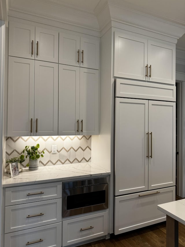 kitchen featuring paneled fridge, decorative backsplash, light stone counters, and white cabinets