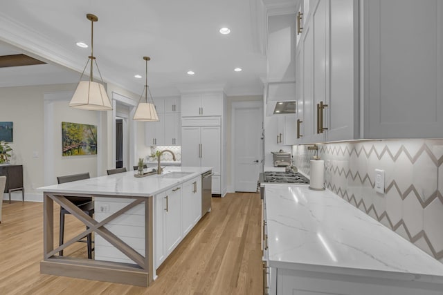 kitchen with sink, tasteful backsplash, decorative light fixtures, a kitchen island with sink, and light wood-type flooring