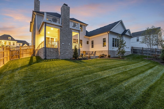 back house at dusk with a lawn and a balcony