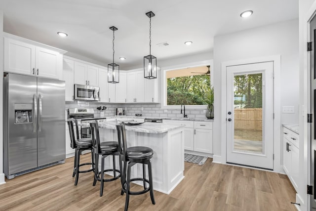 kitchen featuring white cabinetry, stainless steel appliances, light hardwood / wood-style flooring, pendant lighting, and a kitchen island