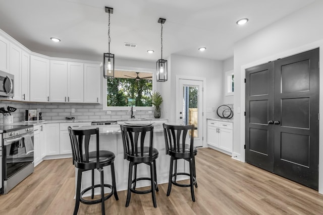 kitchen with decorative light fixtures, stainless steel appliances, white cabinetry, and light hardwood / wood-style floors