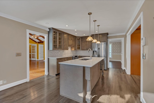 kitchen with sink, dark wood-type flooring, stainless steel fridge, decorative light fixtures, and a kitchen island with sink