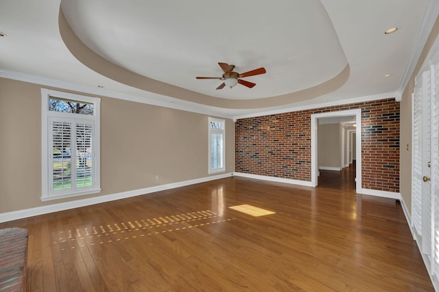 unfurnished room featuring wood-type flooring, a tray ceiling, crown molding, and brick wall