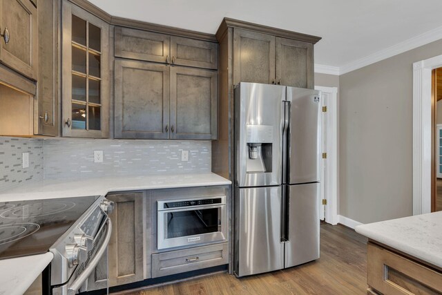 kitchen with light stone counters, dark hardwood / wood-style flooring, decorative backsplash, appliances with stainless steel finishes, and ornamental molding