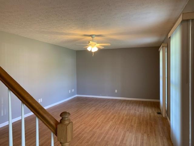 empty room with ceiling fan, light wood-type flooring, and a textured ceiling