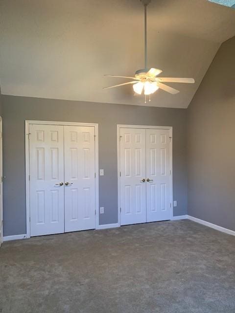 unfurnished bedroom featuring dark colored carpet, ceiling fan, multiple closets, and vaulted ceiling