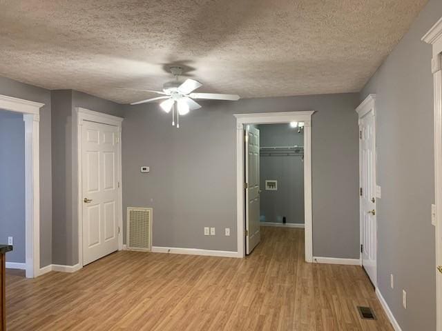 unfurnished bedroom featuring ceiling fan, a walk in closet, light wood-type flooring, and a textured ceiling