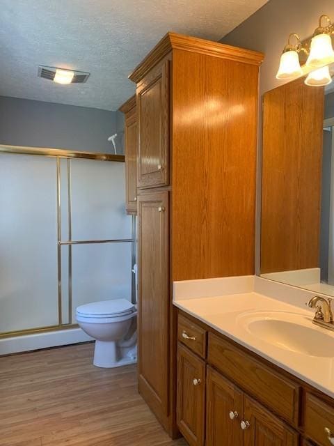 bathroom featuring walk in shower, wood-type flooring, a textured ceiling, toilet, and vanity