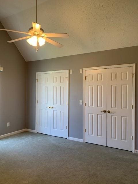 unfurnished bedroom with ceiling fan, a textured ceiling, lofted ceiling, dark carpet, and two closets