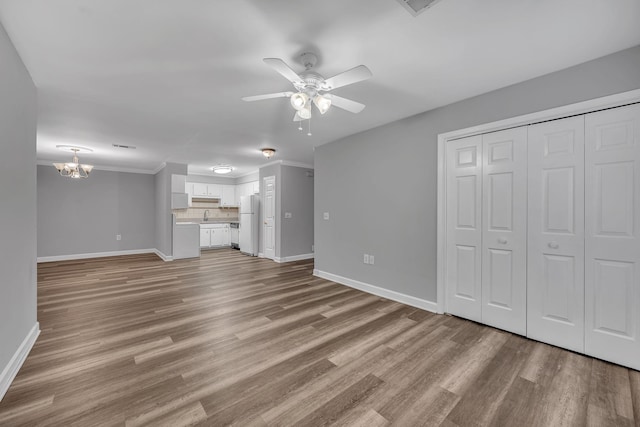 unfurnished living room with ceiling fan with notable chandelier, light hardwood / wood-style floors, crown molding, and sink