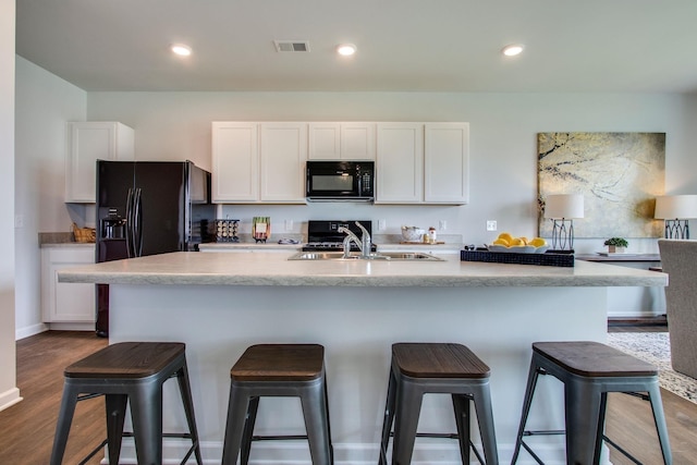 kitchen with a center island with sink, white cabinets, and black appliances