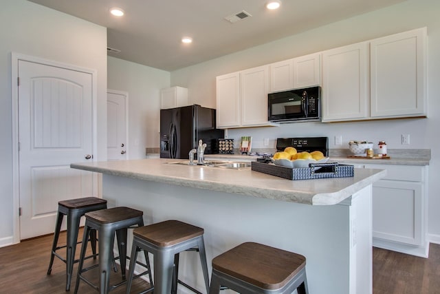 kitchen with a kitchen breakfast bar, a kitchen island with sink, black appliances, white cabinets, and dark hardwood / wood-style floors