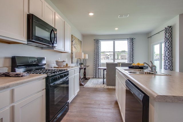 kitchen featuring hardwood / wood-style floors, a kitchen island with sink, black appliances, white cabinets, and sink