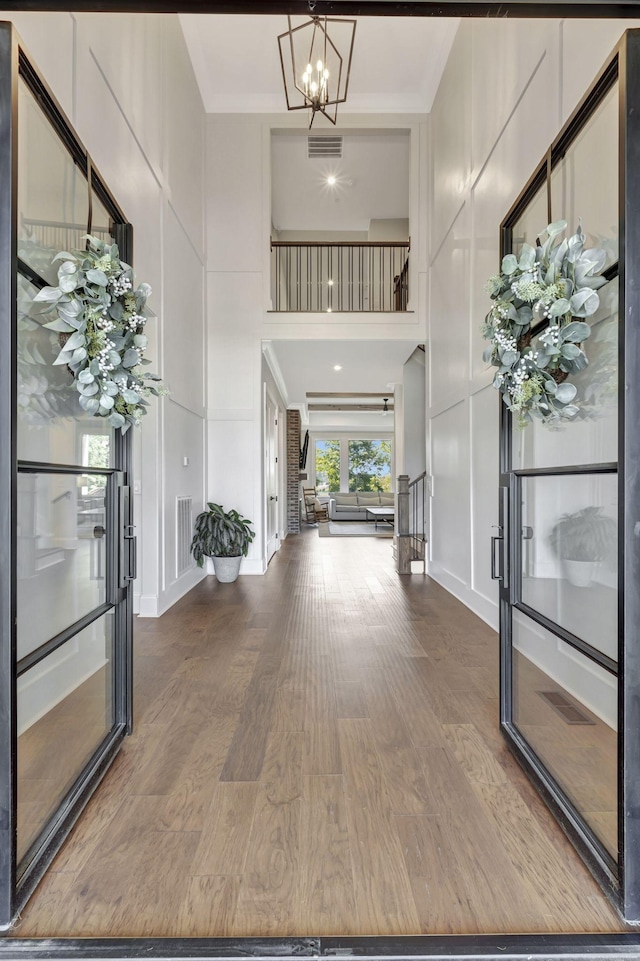 foyer with crown molding, a towering ceiling, hardwood / wood-style flooring, and an inviting chandelier