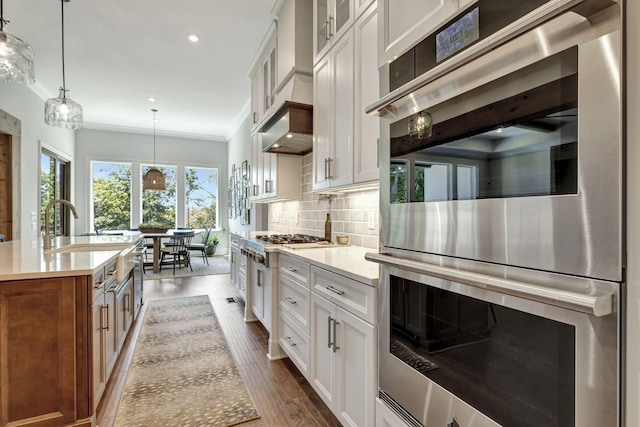 kitchen featuring stainless steel double oven, a center island with sink, white cabinetry, and backsplash