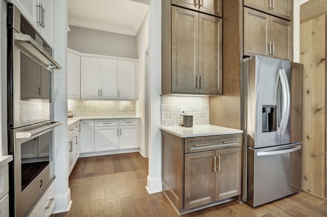 kitchen featuring decorative backsplash, white cabinetry, stainless steel appliances, and light hardwood / wood-style flooring