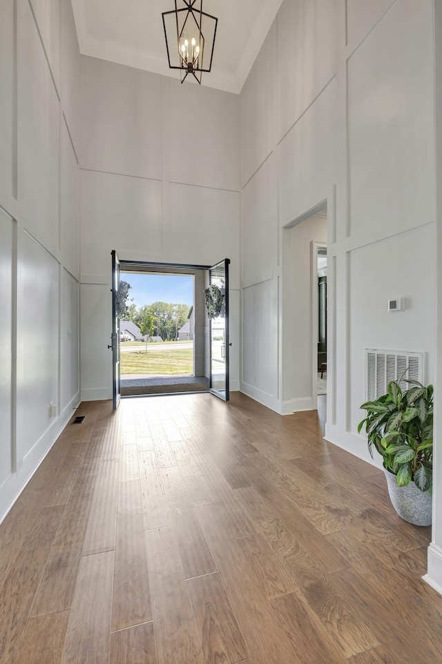 foyer entrance with hardwood / wood-style floors, a towering ceiling, crown molding, and a notable chandelier